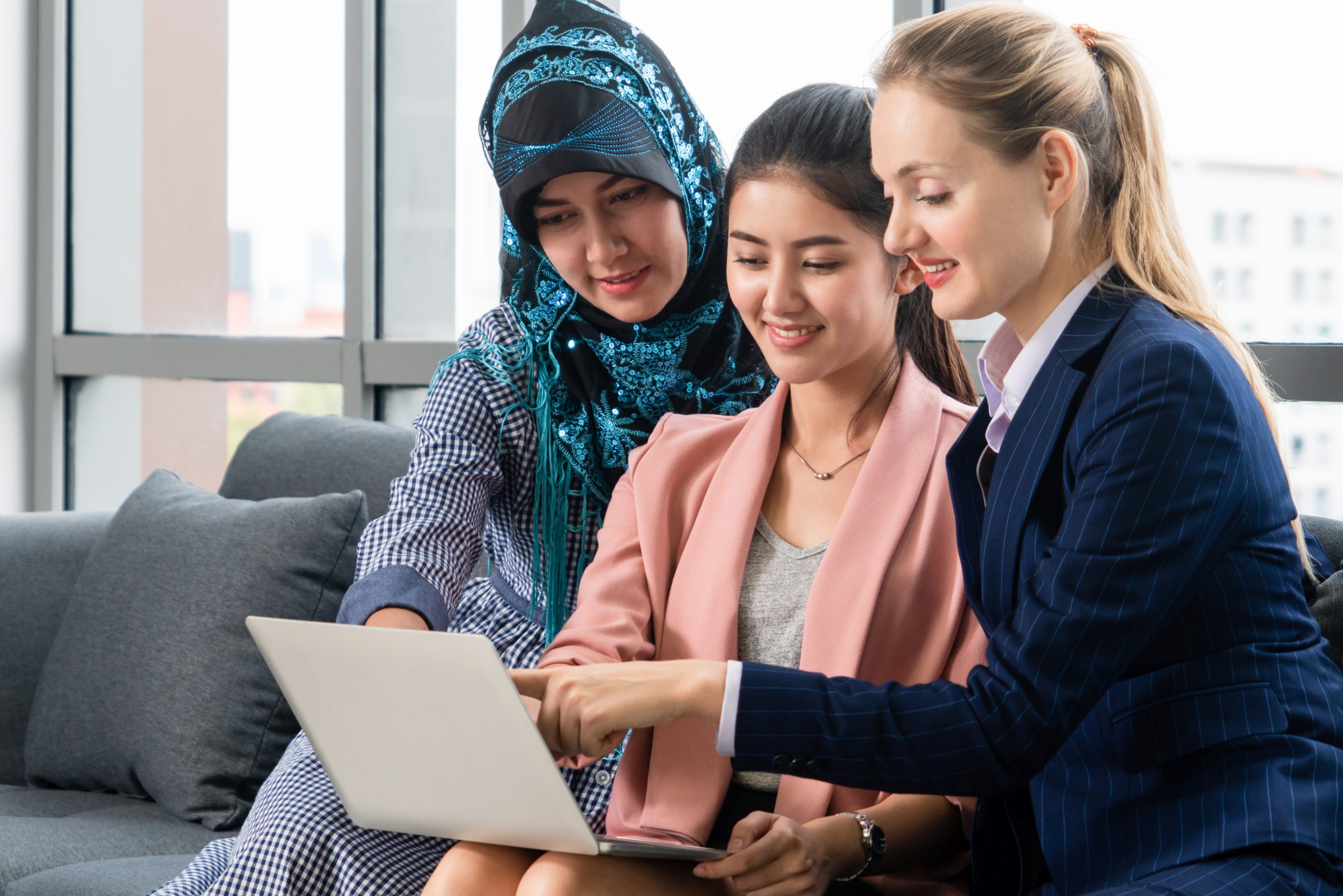 Three women are sitting down with a laptop and are communicating with an interpreter.